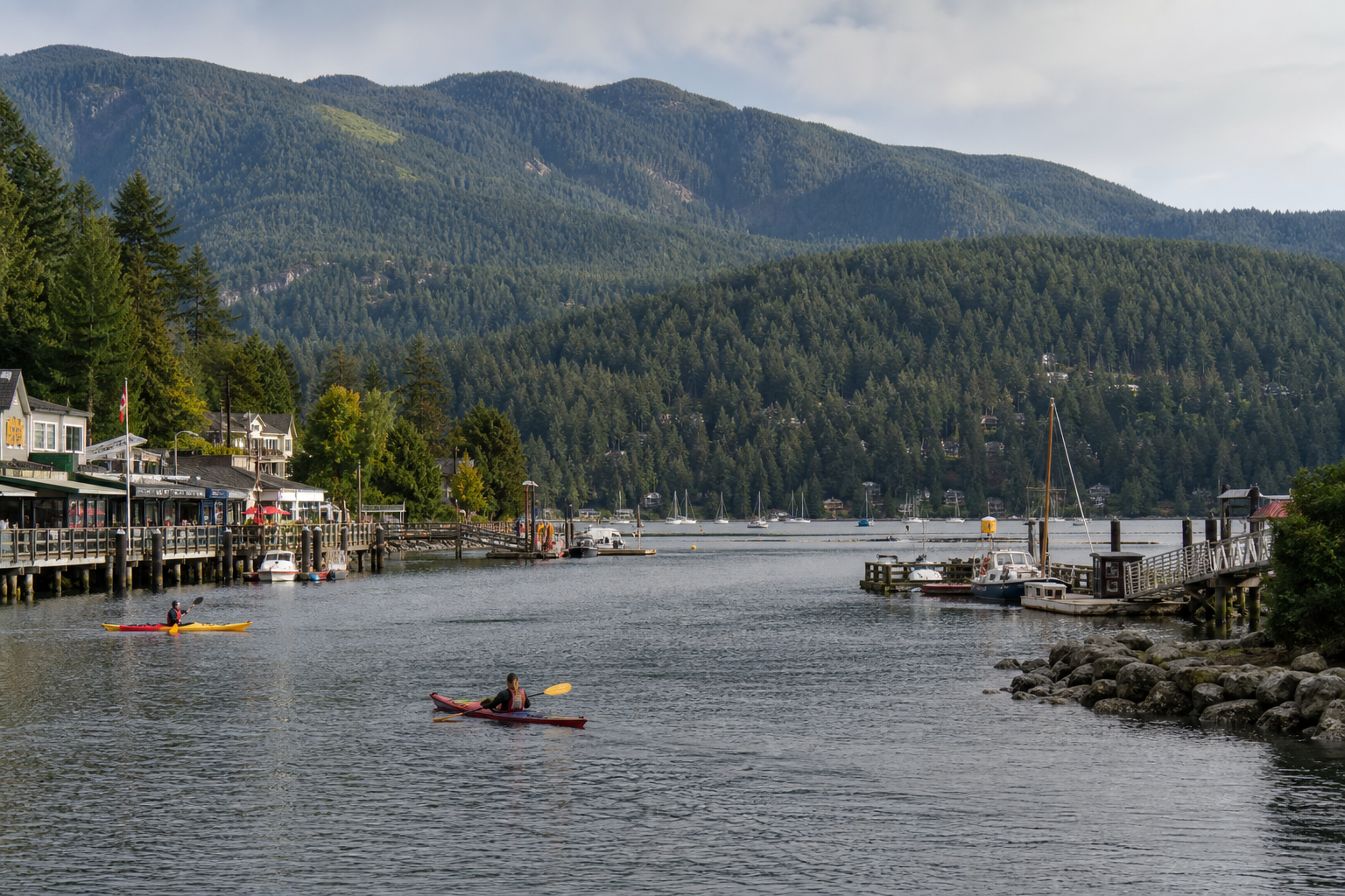 Deep Cove harbour with kayaks on the water in the foreground and cedar-shingled cottages on the slope above, late-afternoon golden light
